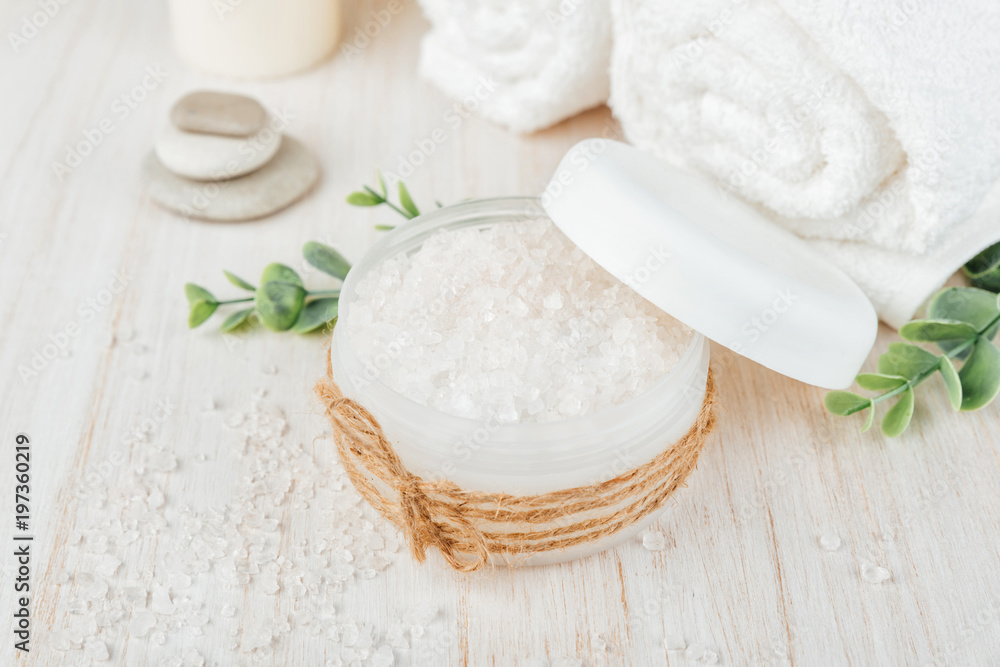 Spa composition on white wooden background. Sea salt, white rolled towels, candles, green herbs Spa composition on white wooden background. Sea salt, white rolled towels, candles, green herbs