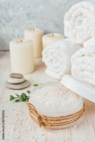 Spa composition on white wooden background. Sea salt, white rolled towels, candles, green herbs