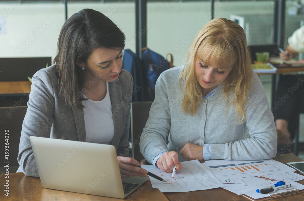 two attractive young woman working together reading and point on paperwork for analysis and using laptop to mentoring about some business planning at coffee shop. two attractive young woman working together reading and point on paperwork for analysis and using laptop to mentoring about some business planning at coffee shop.