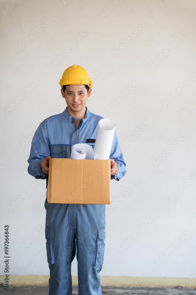 Young Asian technician man with safety helmat carry a brown box of plans. Young Asian technician man with safety helmat carry a brown box of plans.