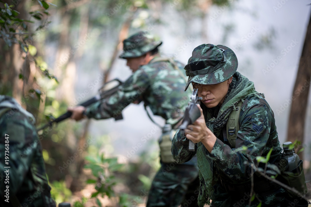 Squad of soldiers patrolling across the forest area and smoke background.