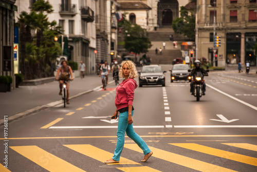 A young curly blonde woman walks across the crosswalk of the road in Lucerne, Switzerland.