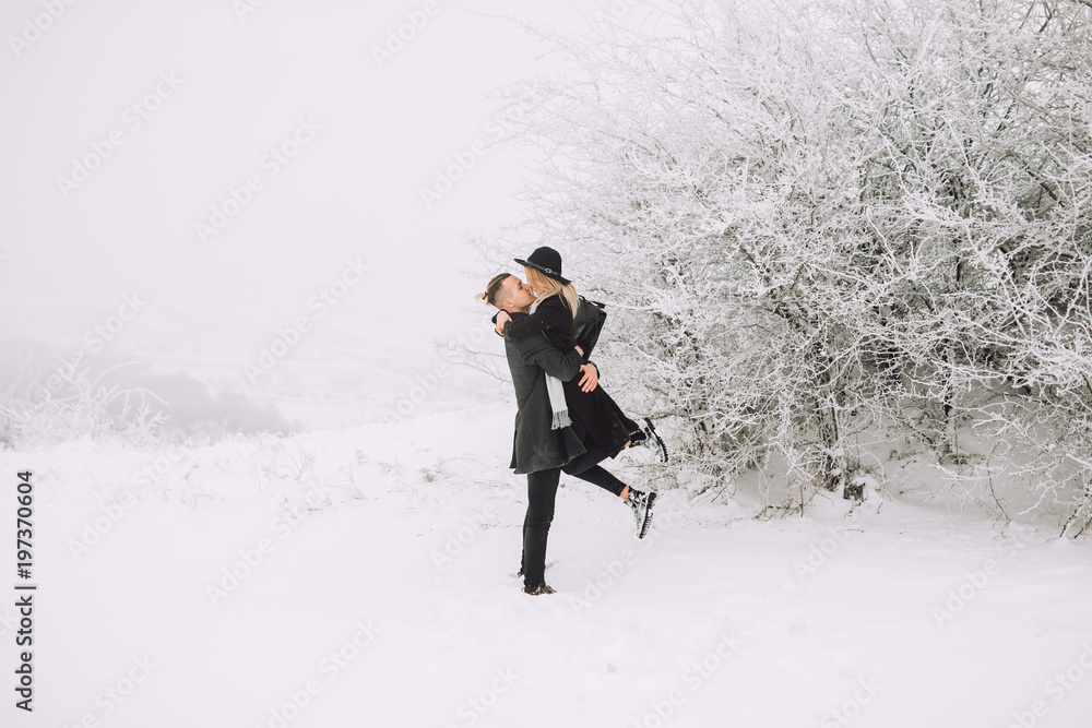 Cheerful couple stands beside a beautiful winter landscape in the forest