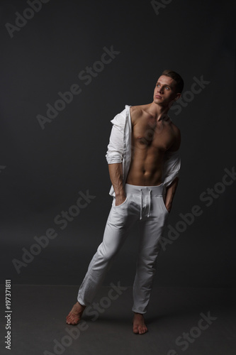a guy with a naked torso, in white pants, and in a white shirt, stands on a gray background