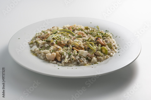 Round white dish of risotto with artichokes and seafood