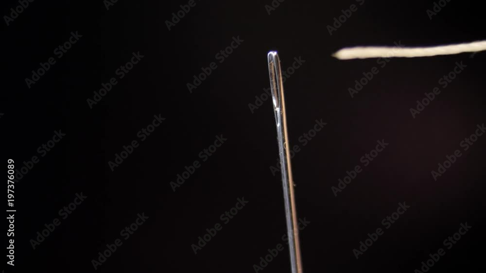 Threading the eye of a needle. Pulling the thread into the needle eye of the sewing needle. Threading the eye of a needle. Pulling the thread into the needle eye of the sewing needle.