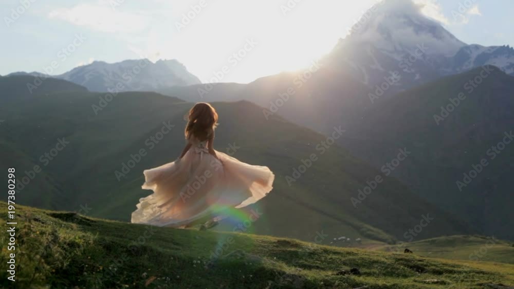 beautiful girl in a chic dress dances in the evening against the backdrop of the mountains and the setting sun