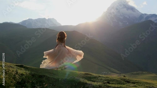 beautiful girl in a chic dress dances in the evening against the backdrop of the mountains and the setting sun