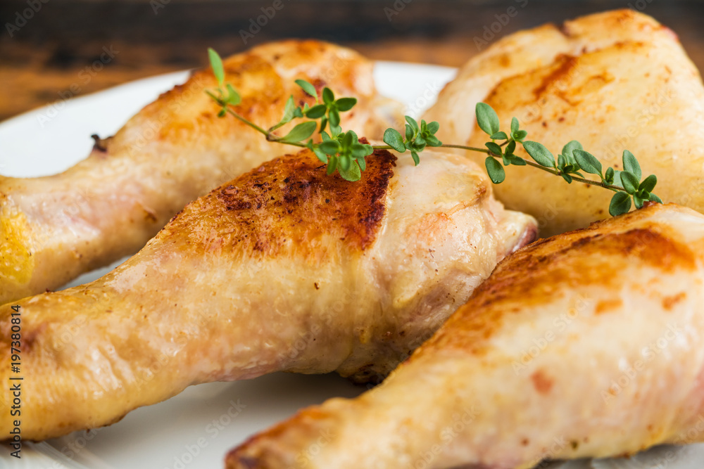 Roasted chicken drumsticks and fresh thyme on a white plate. Roasted chicken drumsticks and fresh thyme on a white plate.