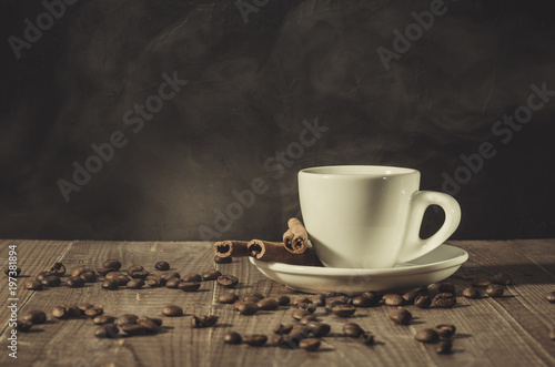 white hot cup of coffee  sticks of cinnamon and coffee beans white hot cup of coffee  sticks of cinnamon and coffee beans on a dark wooden background.