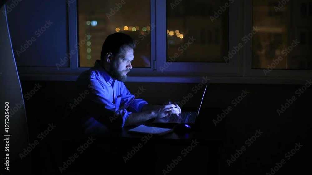 a tired businessman works late in the evening with a laptop in the office and composes a financial report. a tired businessman works late in the evening with a laptop in the office and composes a financial report.
