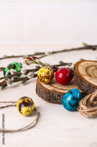 colored quail eggs for Easter and willow branches on white wooden table