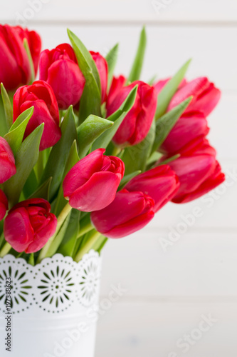 Fresh red tulip flowers bouquet on shelf in front of wooden wall.