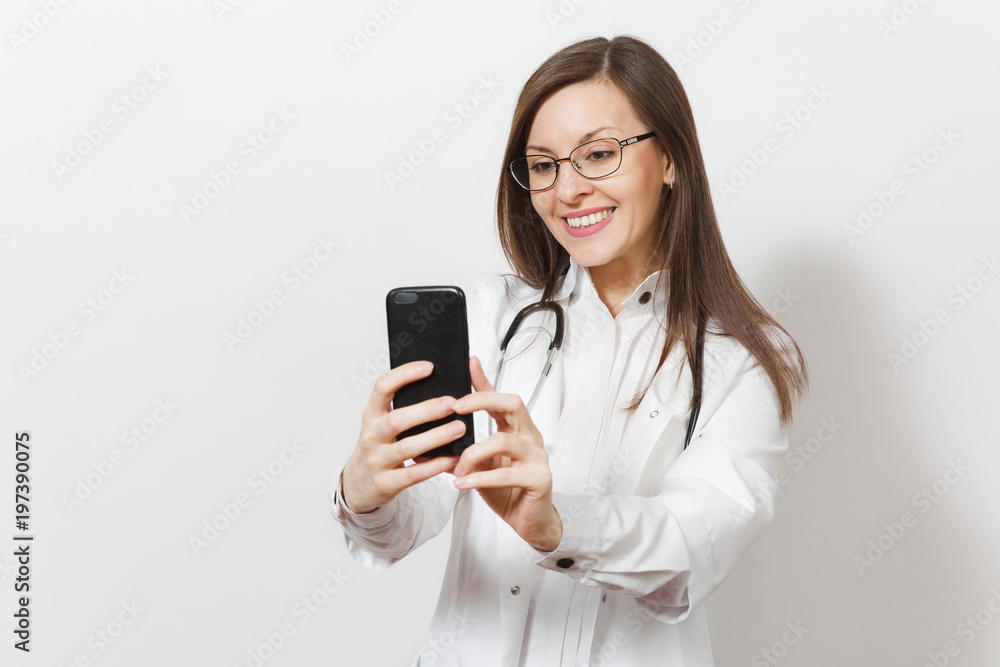 Smiling fun beautiful young doctor woman with stethoscope, glasses isolated on white background. Female doctor in medical gown doing selfie on mobile phone. Healthcare personnel, health, medicine. Smiling fun beautiful young doctor woman with stethoscope, glasses isolated on white background. Female doctor in medical gown doing selfie on mobile phone. Healthcare personnel, health, medicine.