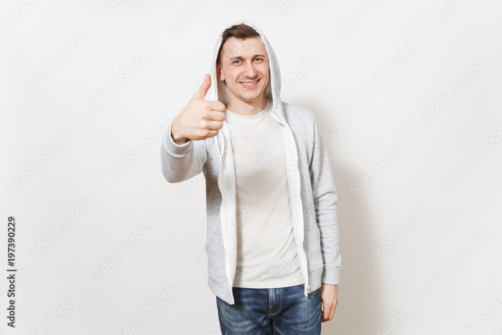 Young handsome smiling man in t-shirt, blue jeans and light sweatshirt shows gesture thumbs up and rejoices isolated on white background. Concept of emotions, good mood. Copy space for advertisement. Young handsome smiling man in t-shirt, blue jeans and light sweatshirt shows gesture thumbs up and rejoices isolated on white background. Concept of emotions, good mood. Copy space for advertisement.