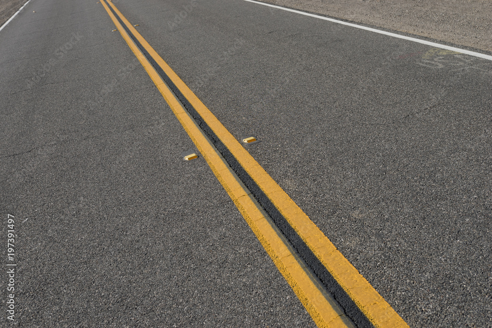 Center of long black asphalt yellow lines in roadway.