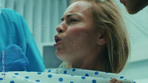 Close-up on a Face of a Woman in Labor Pushing Hard to Give Birth, Obstetricians Assisting, Spouse Holds Her Hand. Modern Maternity Hospital with Professional Midwives. 