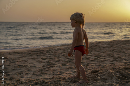 Little boy three years old on the background of the sea and sunset