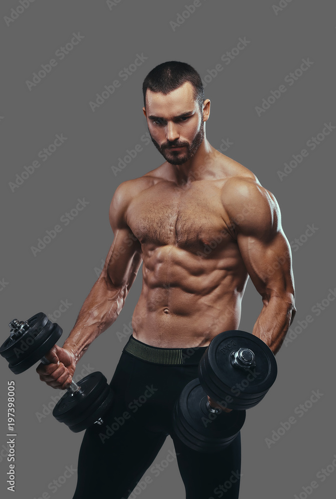 A Muscular guy working out with dumbbells. Isolated on a gray ba