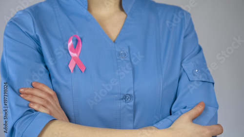 Female physician with pink ribbon in blue uniform, breast cancer awareness