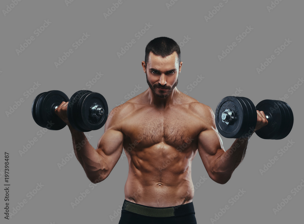 A Muscular guy working out with dumbbells. Isolated on a gray ba