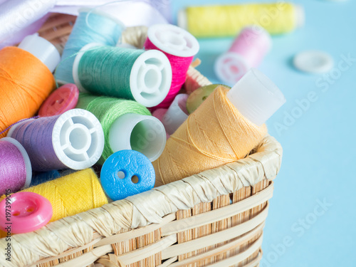 Colorful sewing buttons and thread in a wooden box on a blue background.