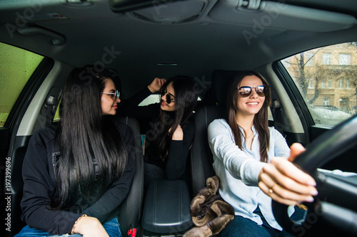 Just keep driving. Three beautiful young cheerful women looking away with smile while sitting in car