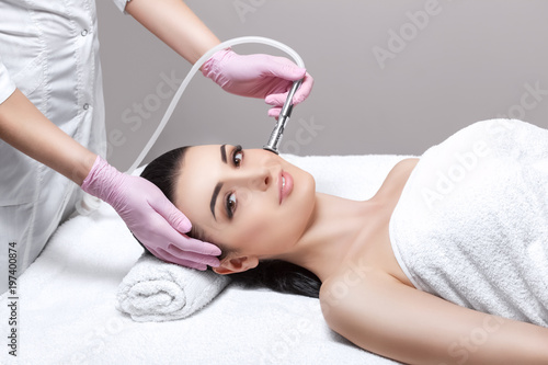 The cosmetologist makes the procedure Microdermabrasion of the facial skin of a beautiful, young woman in a beauty salon.Cosmetology and professional skin care.