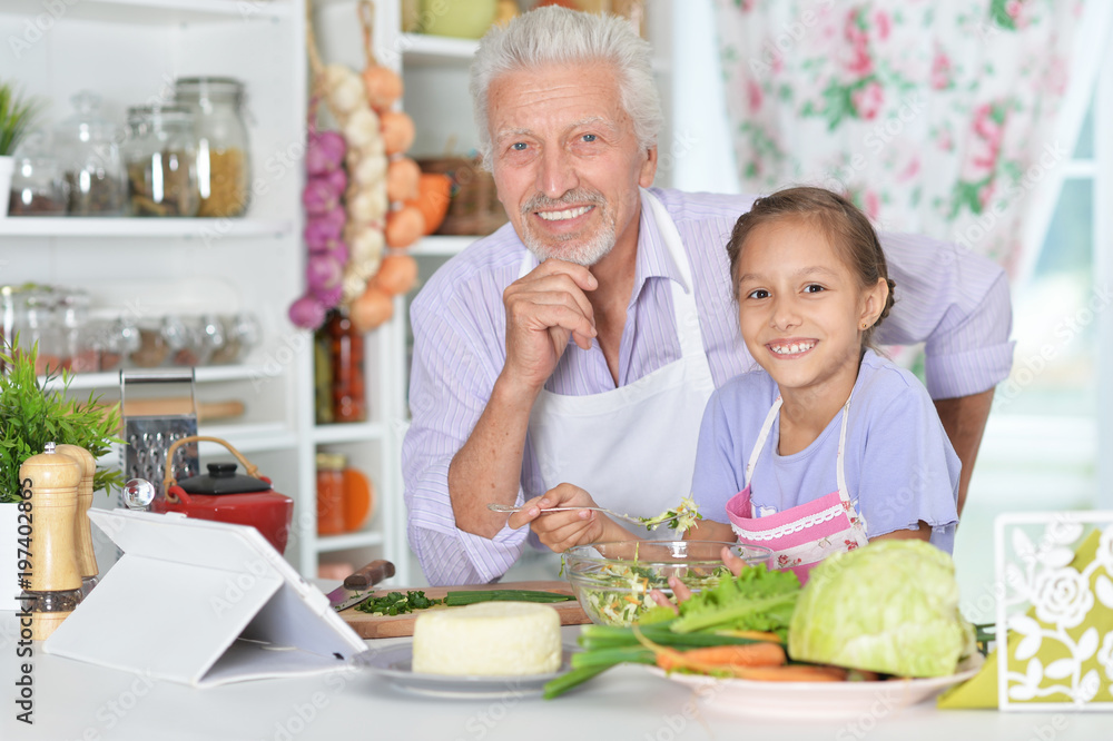 Senior man with granddaughter preparing dinner in kitchen