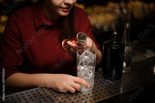 Side view of female bartender pouring some gin into a cocktail glass