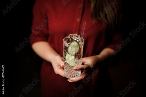 Woman holding a cocktail glass with fresh alcoholic drink with cucumber slices and gin