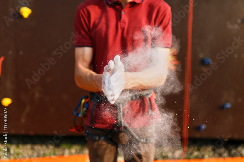 Close up of climber man coating hands in powder chalk magnesium and preparing to climb outdoor training rock wall. Powder in the air after clapping hands
