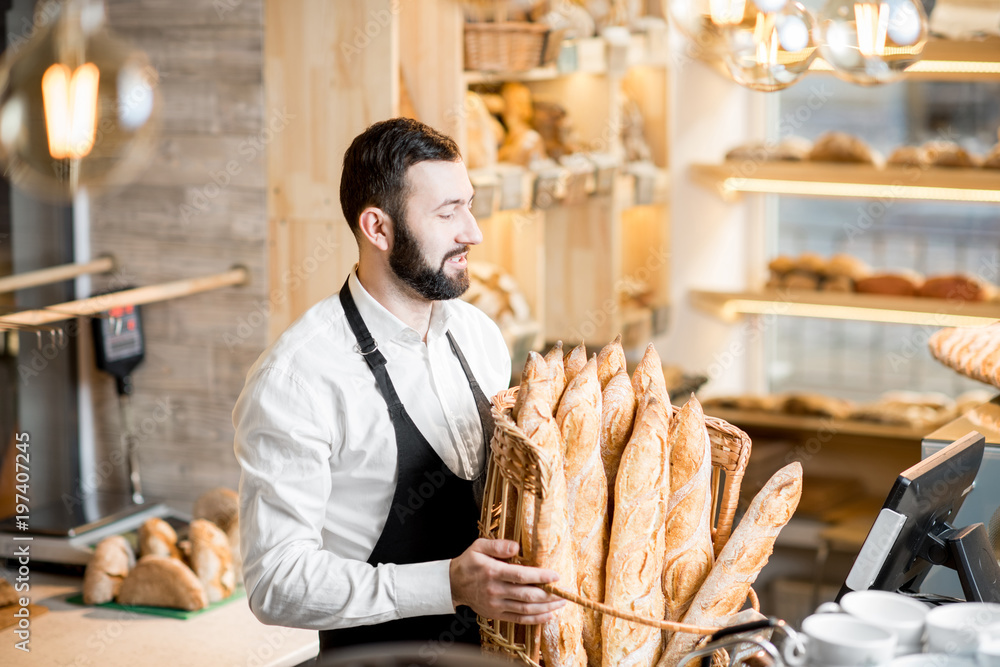 Handsome bread seller with basket full of baguettes in the beautiful store with bakery products