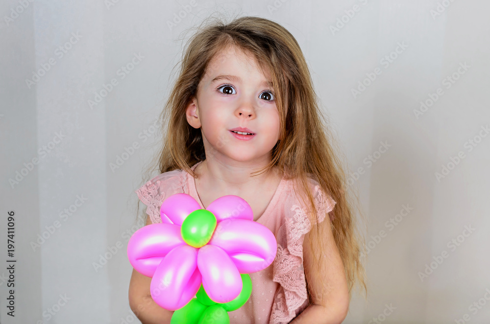 the little girl made surprised big brown eyes, looks straight and holds a pink inflatable flower made of long balloons the little girl made surprised big brown eyes, looks straight and holds a pink inflatable flower made of long balloons