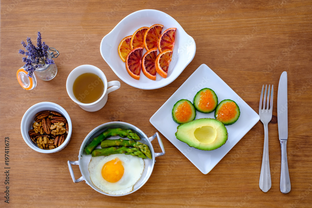Table servie par les plat (oeuf, legumes, oeufs de saumon, noix, orange sanguine, thé vert). Repas type paleo, sans gluten, low carb. Top vue.