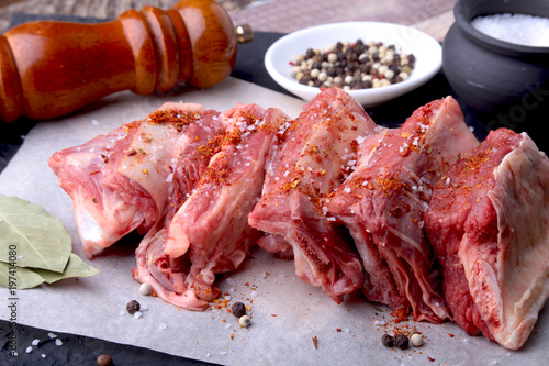 Raw fresh meat, uncooked lamb or beef ribs with pepper, garlic, salt, bay leaves and spices on dark stone background, Ready for cooking. copy space.