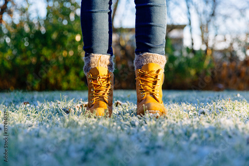 Two female feet in orange shoes standing on frozen grass. Iceland, Reykjavik.