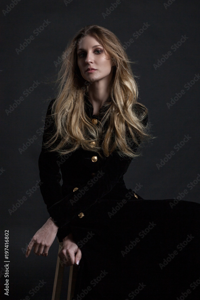 Full length model in black dress posing sitting on dark background Full length model in black dress posing sitting on dark background