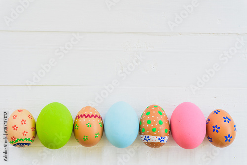 Happy easter! Row Colorful Easter eggs with colorful paper flowers on white wooden background.