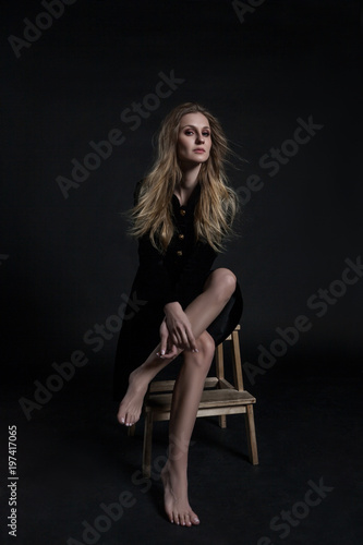 Full length model in black dress posing sitting on dark background