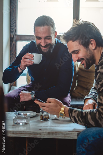 Smiling friends drinking coffee and looking at the mobile phone