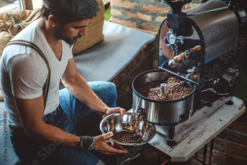 Hipster catching roasted coffee from the roaster with a dish photo