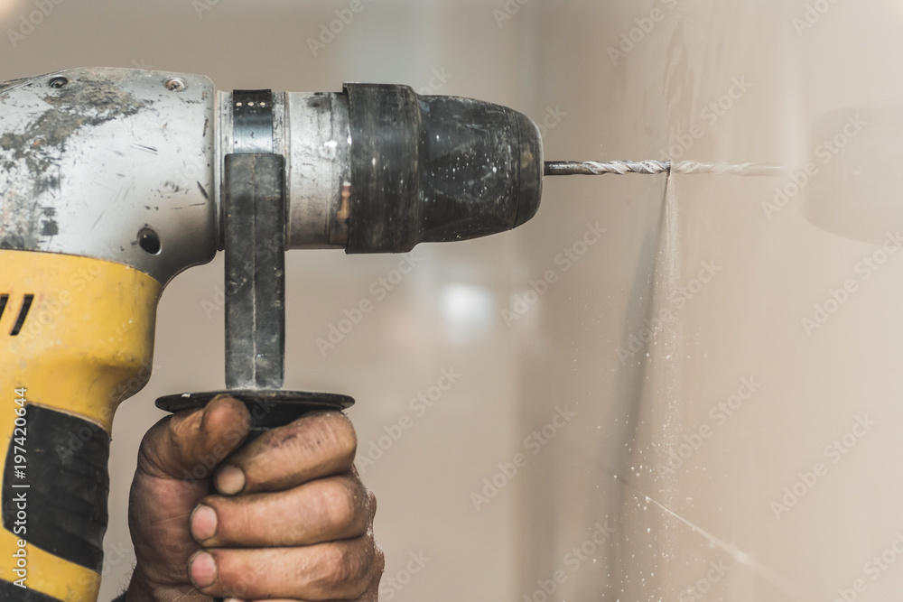A drilling machine is making a hole on a wall of tiles. The worker