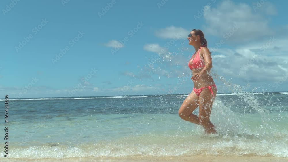 SLOW MOTION CLOSE UP: Happy young woman in pink swimsuit running on sandy beach, splashing ocean water. Smiling girl enjoying fun vacation in tropical island on sunny day. Exotic travel destination SLOW MOTION CLOSE UP: Happy young woman in pink swimsuit running on sandy beach, splashing ocean water. Smiling girl enjoying fun vacation in tropical island on sunny day. Exotic travel destination