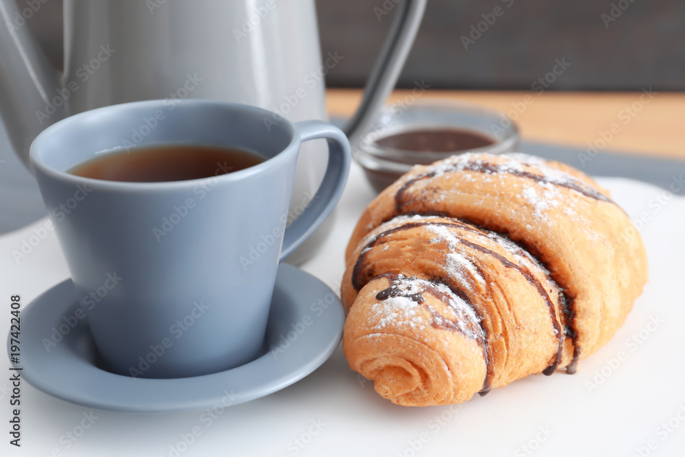 Tasty croissant near cup of coffee on table