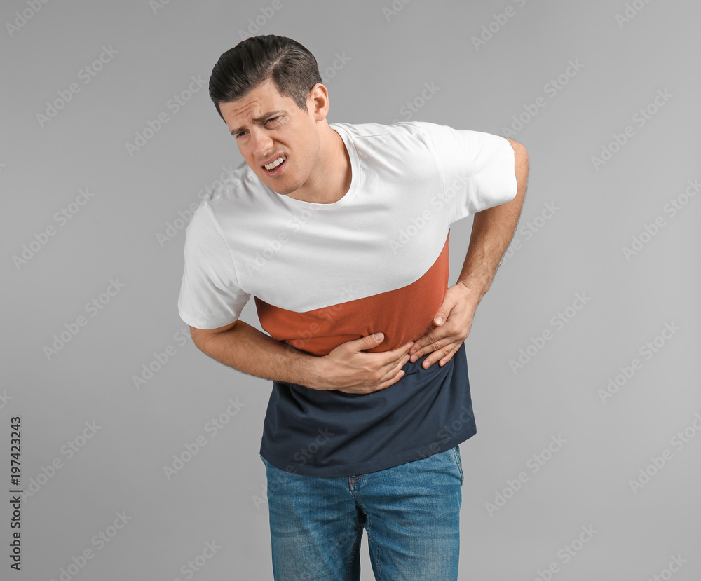 Young man suffering from abdominal pain on grey background Young man suffering from abdominal pain on grey background