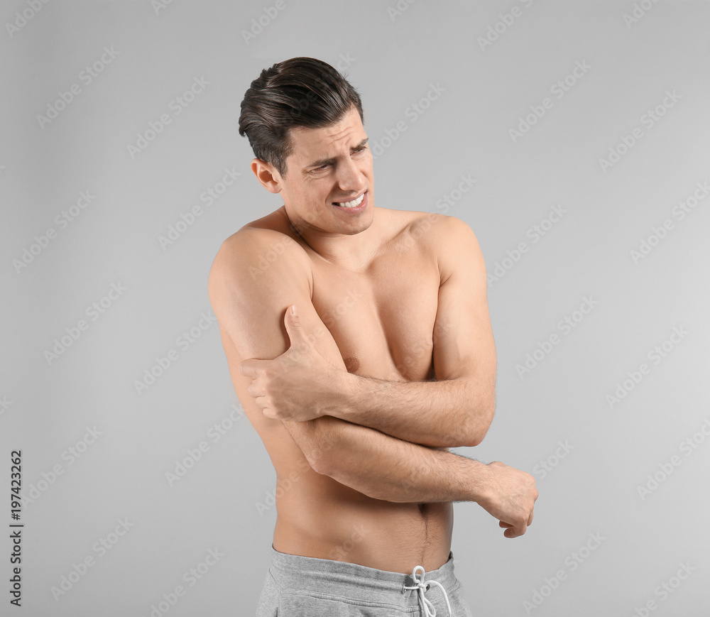Young man suffering from pain in arm on grey background Young man suffering from pain in arm on grey background