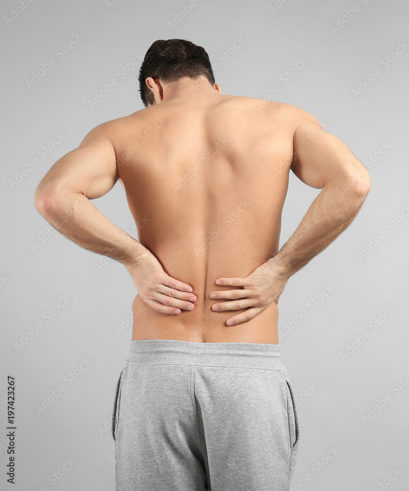 Young man suffering from back pain on grey background Young man suffering from back pain on grey background