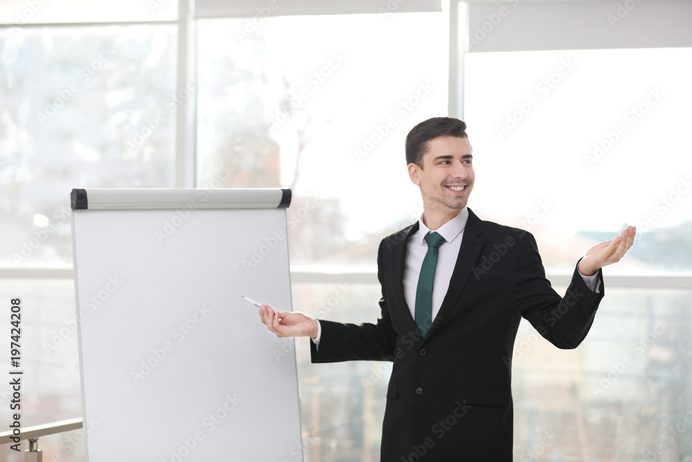 Business trainer giving presentation on flip chart board indoors Business trainer giving presentation on flip chart board indoors