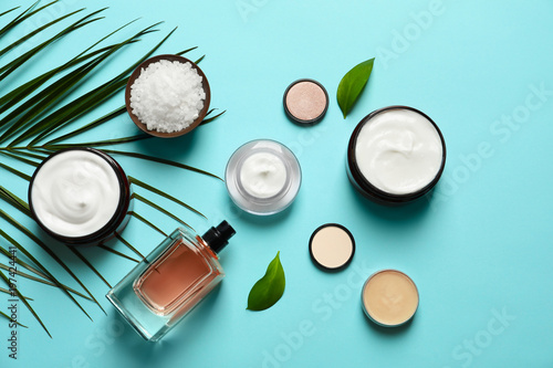 Different skin care cosmetic products with green leaves on color background  top view